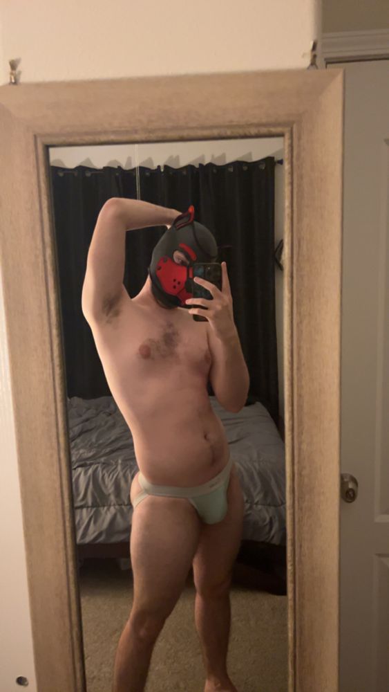 Atlas standing in front of a mirror with his pup hood and jock strap on ready to get in the sub muscle headspace