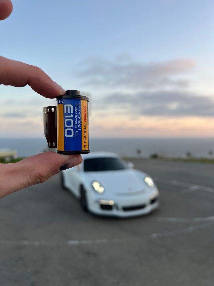 Roll of Kodak ektachrome held against an out of focus background of a car with a sunset behind it
