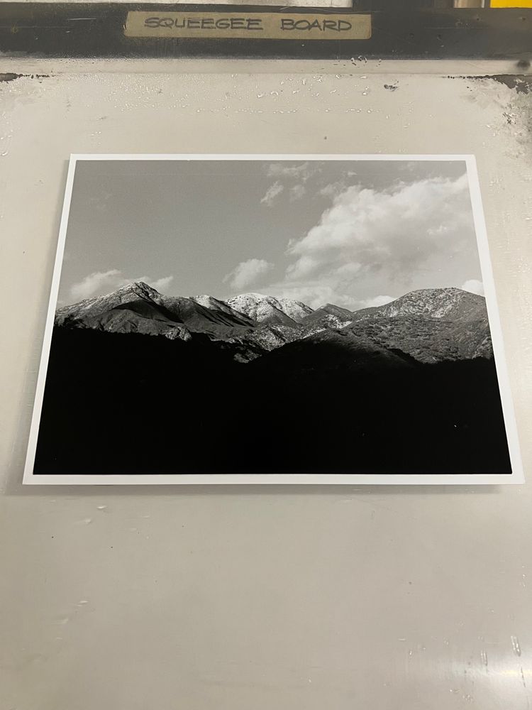 Black and white composition of mountains with a clear sky with clouds on the left. The foreground is dark, the mountains fill the mid ground, and the sky and clouds set a cheerful tone in the back