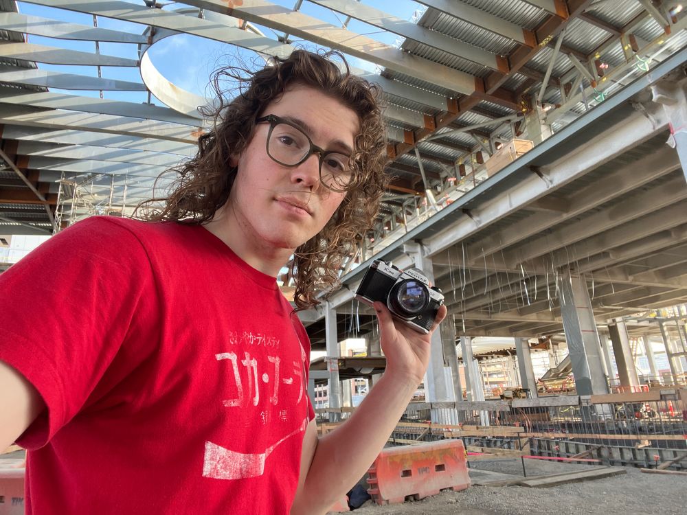 Figure in red shirt with long curly hair holding up a camera in a construction site