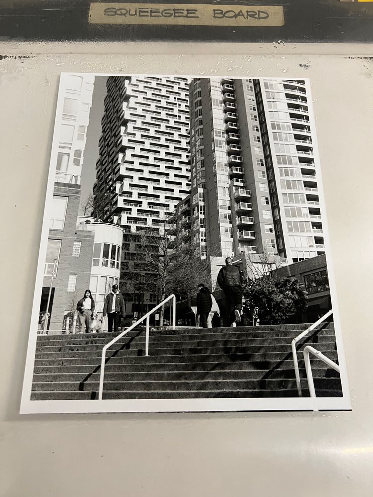 A black and white architectural composition. Figures use stairs in the foreground against a background of complex shapes formed by the windows of modern buildings