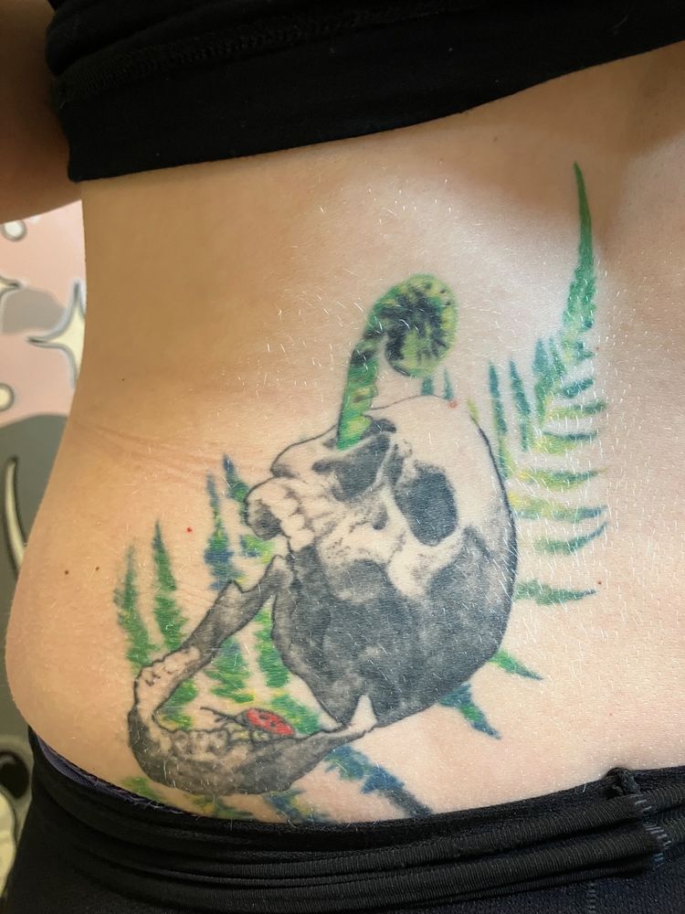 Tattoo guéri d'un crâne avec une fougères entre la hanche et la colonne vertébrale.