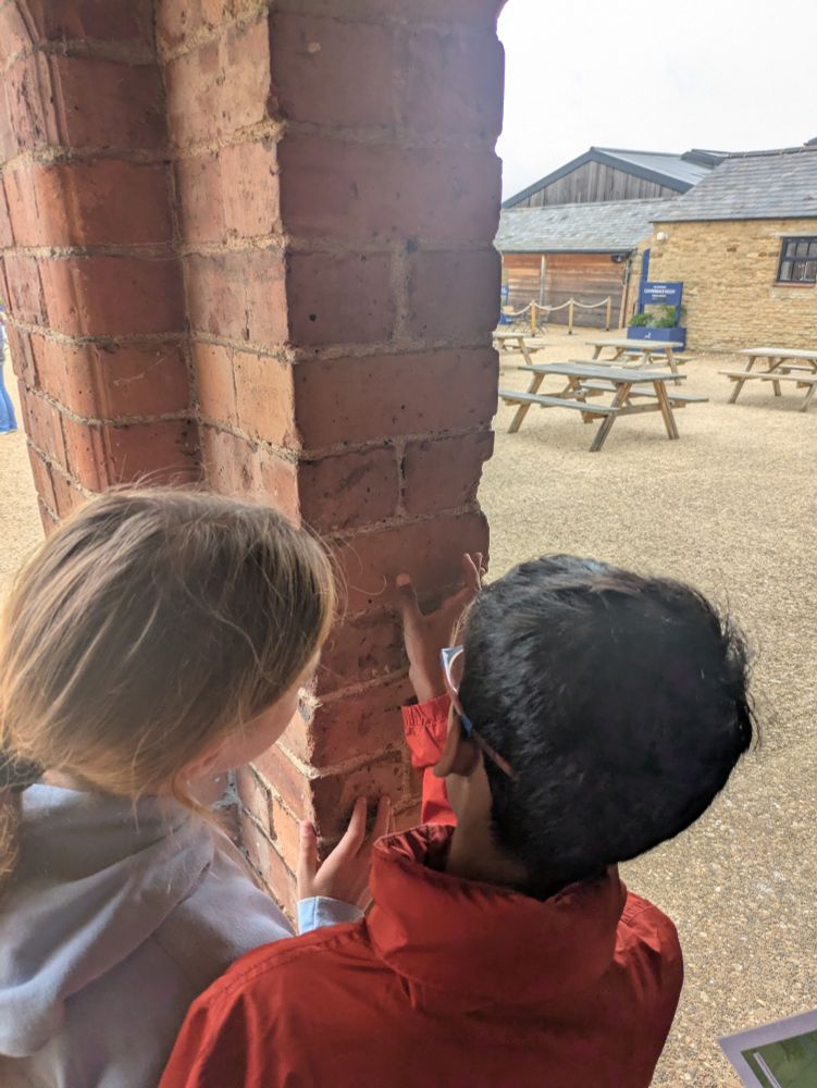 Two children looking at fingerprint in a brick column
