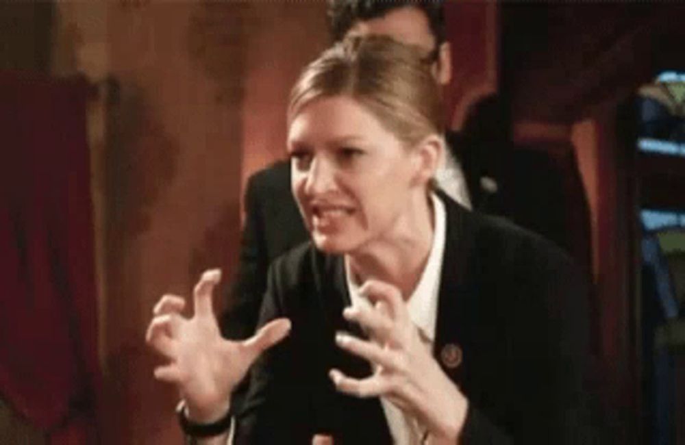 a woman in a suit and white shirt is making a funny face with her hands in the air .