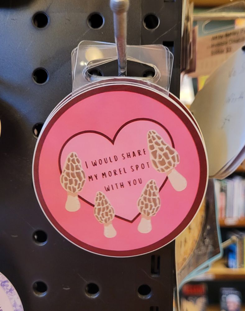A round pink sticker with a heart surrounded by four morel mushrooms. The text reads: I would share my morel spot with you. Art by wide.eyed.outside