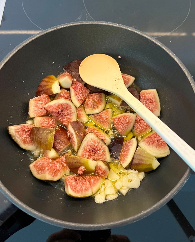 Eine Pfanne mit Olivenöl, Knoblauch und geviertelten Feigen. 