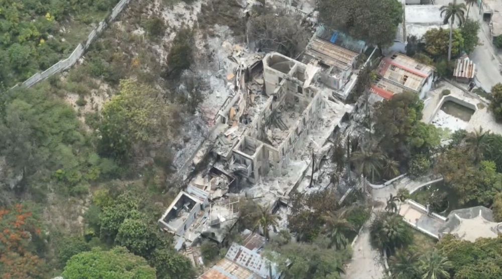 Drone image of the Hotel Oloffson, Port-au-Prince, with the entirety of the wooden building burned, only the brick skeleton remains, surrounded by trees.