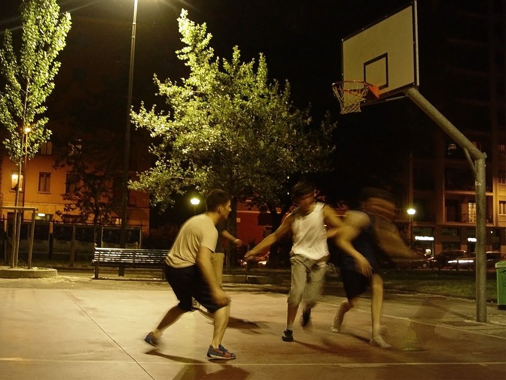 Four guys playing basketball late in the evening on an outside court in Milan, Italy.