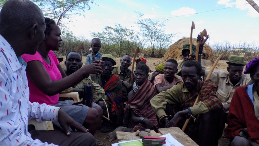 Turkana research assistant Amuria Lotiira holds a saliva collection tube and explains the protocol to potential participants in an ASU study. In 2015, a team tested levels of cortisol and testosterone from saliva samples from Turkana pastoralist warriors in Kenya. A Turkana-area chief sits to the left of Lotiira. Photo by Matthew Zefferman