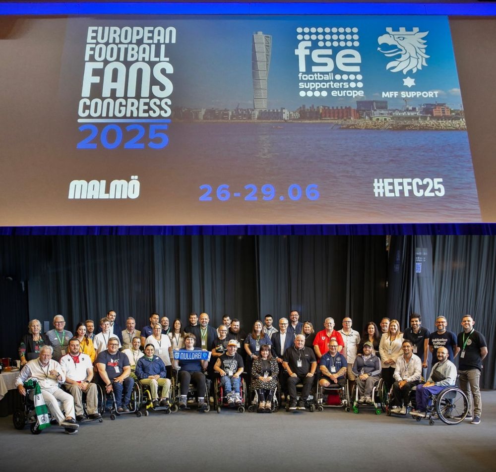 Image description: A group photo of disabled football supporters, with the FSE, UEFA, Ted Morris of LFCDSA and other delegates. Above that is the main screen at the European Football Fans Congress 2025.