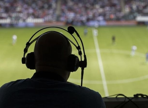 Image description: A back view of a commentator looking over a pitch, with a headset on.