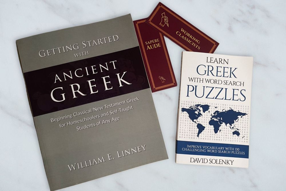 A copy of the book Getting Started with ancient Greek by William E. Linney and the book Learn Greek with Wordsearch Puzzles. Also pictured are two Working Classicists bookmarks.