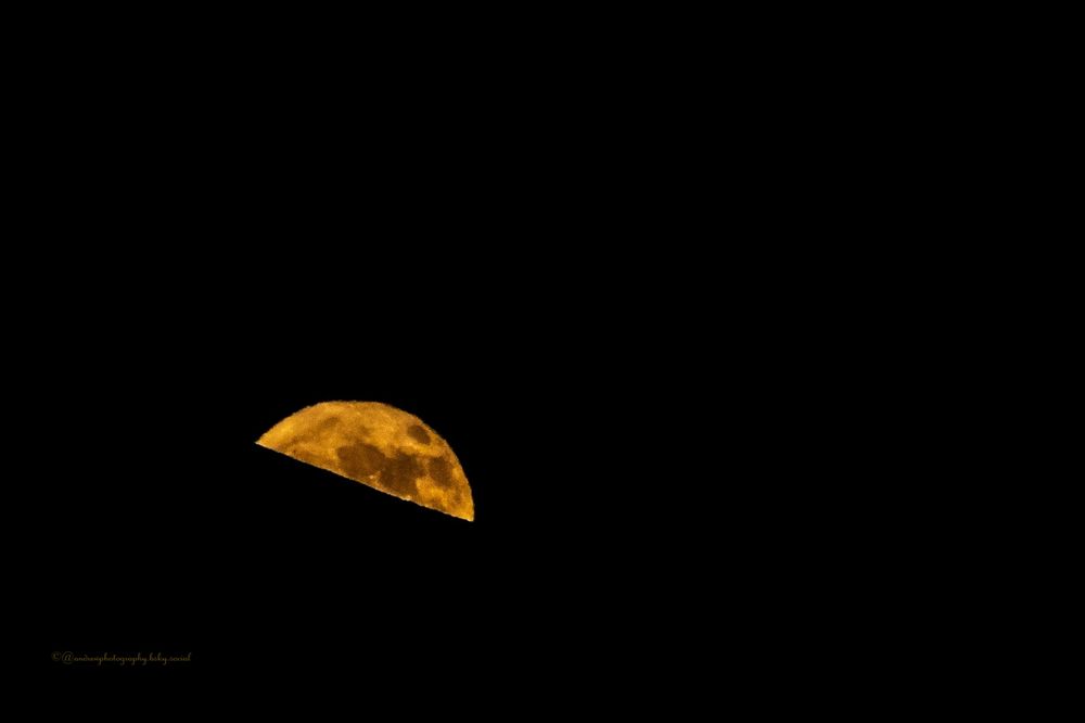 Golden Crescent Emerges:
A luminous golden crescent moon emerges from behind a mountain silhouette, its cratered surface glowing like molten amber against the velvet black night sky, with intricate lunar features clearly visible