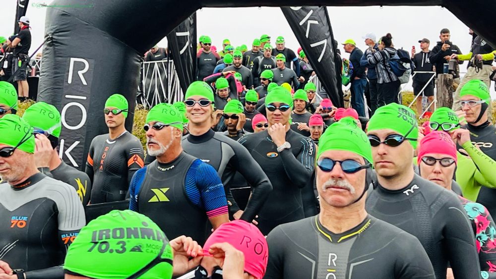 This photograph captures the pre-race atmosphere at the 2023 Morro Bay Half Triathlon, showing dozens of athletes walking to the water's edge for the swimming leg. The participants wear bright green swim caps that create a vivid sea of color, along with dark wetsuits and goggles essential for the open water swim.
The scene shows athletes of various ages and experience levels, all sharing the same focused anticipation before entering the water. ROKA-branded equipment and wetsuits are visible throughout the crowd, indicating professional organization and sponsorship.
The inflatable archway marks the official start area, while the overcast Central California coast conditions create perfect lighting for the photograph. This moment captures the unique blend of individual determination and collective experience that defines triathlon events, where athletes must transition from this crowded start to the solitary challenge of open water swimming in Morro Bay's waters.