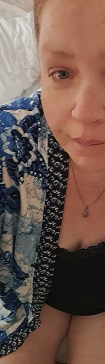 Alte Frau in schwarzem Top, gemustertem Kimono, verquollen in die Kamera schauend, halbes Gesicht, leichtes Lächeln, im Hintergrund weiße Bettlaken