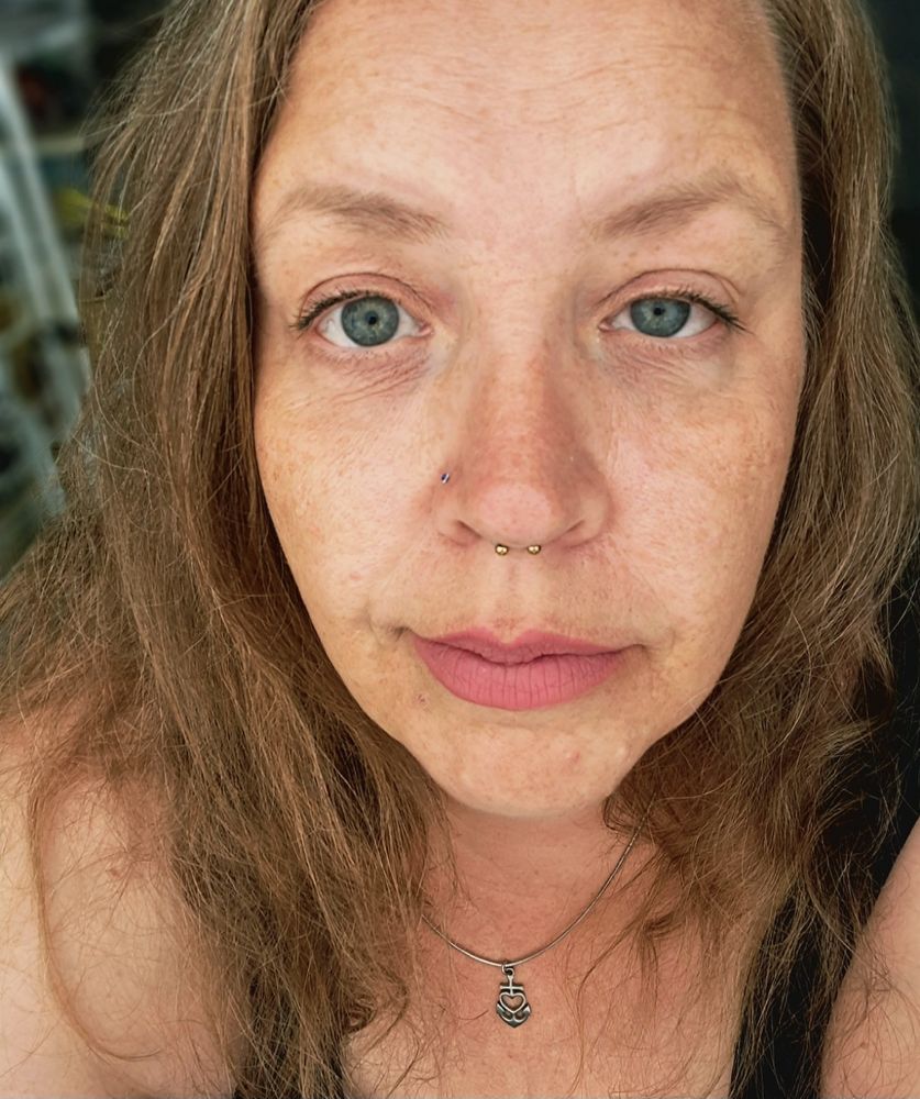 Müde, alte Frau mit Falten, Sommersprossen, und so Gesöns, zwei Piercings der Nase, leichtes Lächeln, im Top, in die Kamera schauend