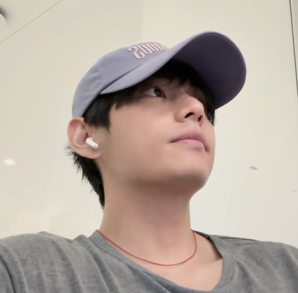 screenshot from tae's vlog in LA, he's wearing a grey shirt, baseball cap and a thin string of red on his neck