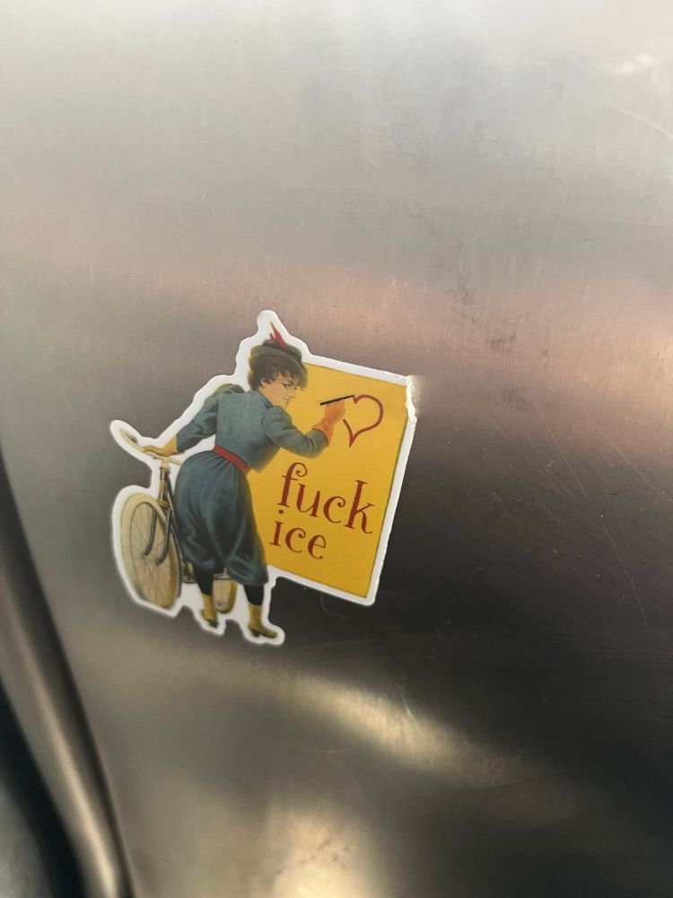 Metal setback with sticker of woman in dress holding bicycle painting heart with “fuck ice” written below