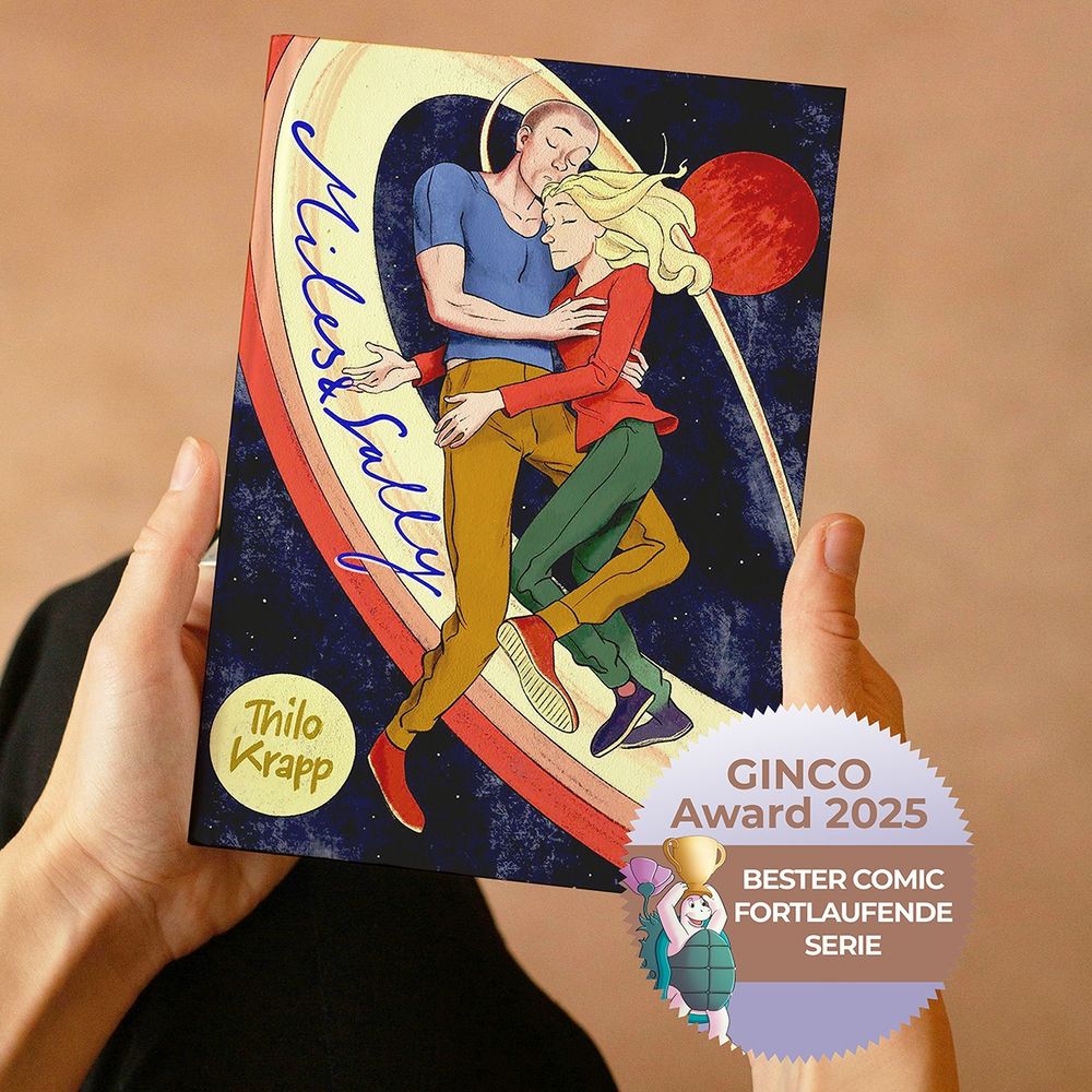 Cover von MILES [&] SALLY, einem webcomic von Thilo Krapp, mit der Plakette des Gewinns der Serie in der Kategorie „Beste fortlaufende Serie“ des GINCO-Awards. Der Buchblock mit der Titellillustration – zwei Figuren in Umarmung, vor einem Weltraum-Hintergrund mit Saturnringen schwebend – wird aus der Vogelperspektive gezeigt mit zwei Händen, die ihn über dem Schoß halten.