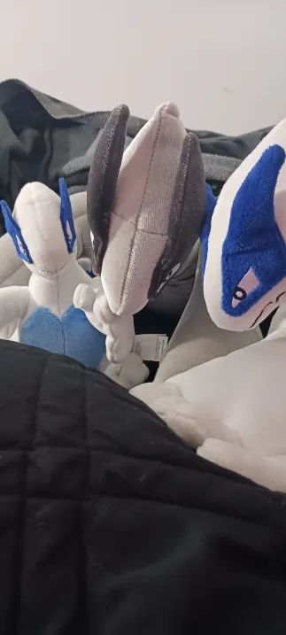 image of official Lugia plushies including a sitting cutie plushie, a 25th anniversary silver lugia plushie and a standard Lugia plushie