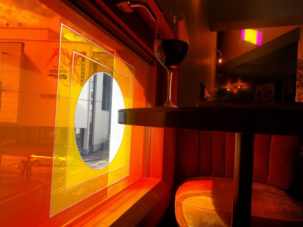 Picture Palace / Pálás bar sitting at a table with a glass of wine and one of the many stained glass windows is at table height with red orange and yellow light