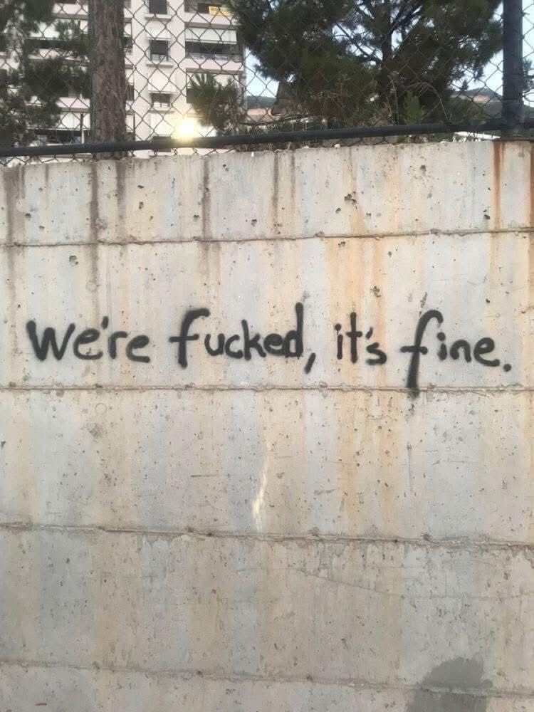 Graffiti on a pale concrete wall that reads "We're fucked, it's fine." 
