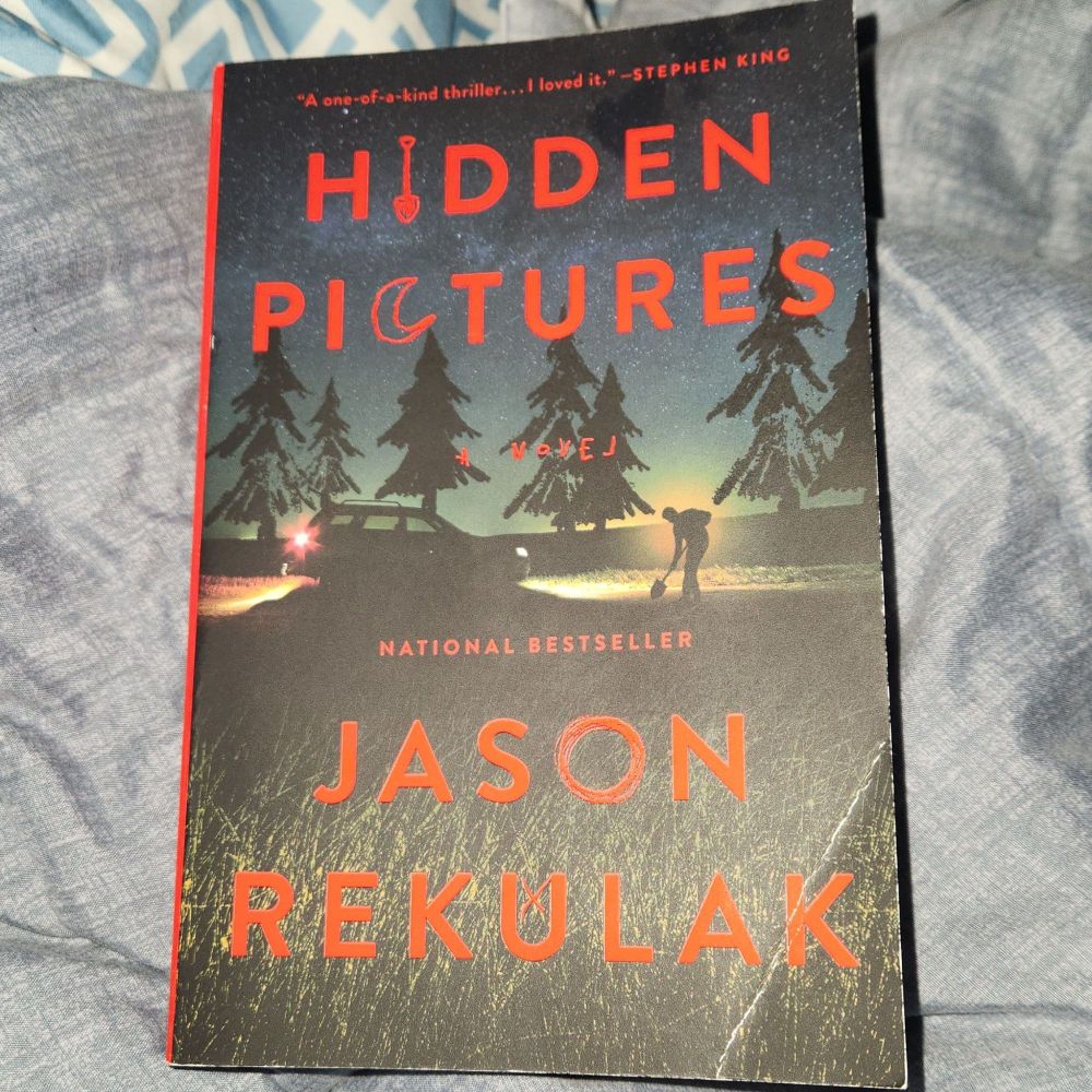 A photo of the novel "Hidden Pictures" by Jason Rekulak. The I in Hidden has a shovel, and the C in Pictures has a moon. The illustration depicts a man in front of his car digging a hole with the help of his headlights.