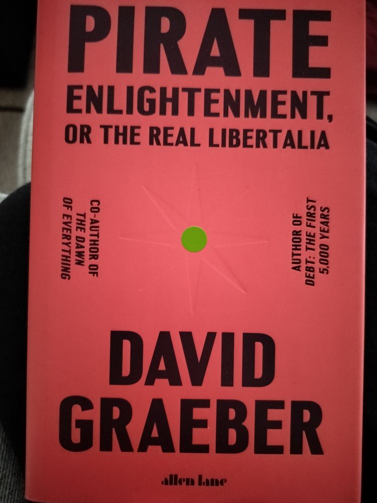 The cover of the book, "Pirate Enlightenment, or the Real Libertalia" by David Graeber. The cover is red with debossed black lettering, and a debossed 8-sided star with a green circle in the middle.