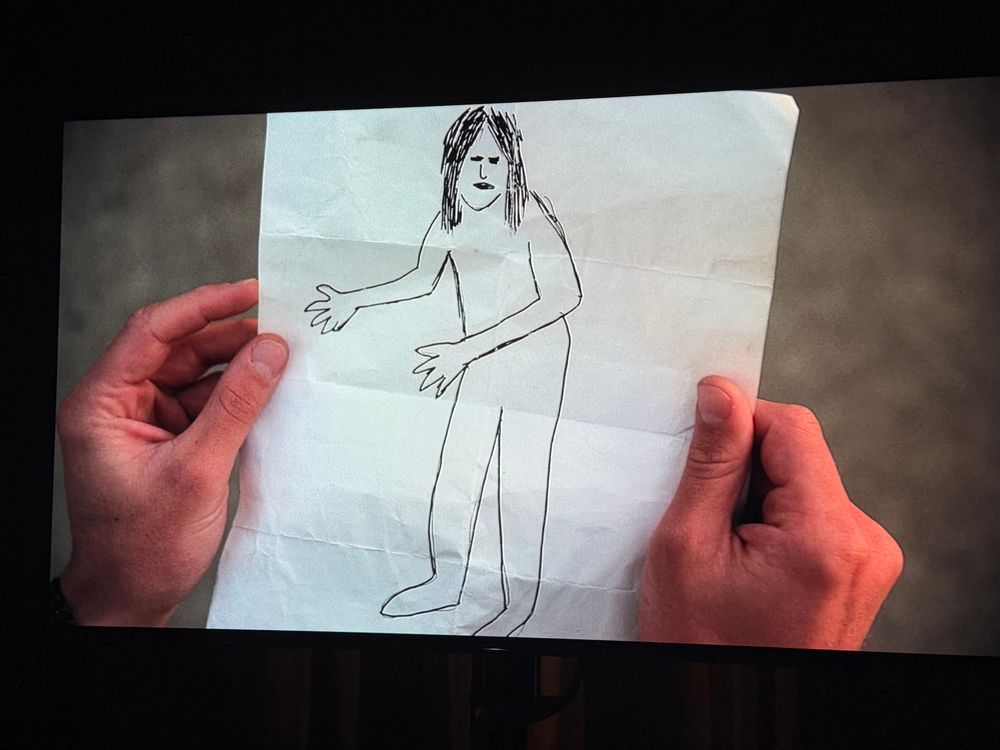 A still from the Jersey Devil episode of X Files showing a sketch Mulder has just been handed by an unhoused gentleman in the outskirts of Atlantic City. The gentleman has confided to Agent Mulder that he has seen The Jersey Devil and he had the foresight to capture the legendary cryptid’s image using the power of illustration. The drawing is straight up just a dude. The only way a verbal thinker can try to explain why the drawing is funny is to explain how I believe a person would realistically react to this drawing upon being handed it by someone in an alley versus how Mulder reacts. In the show, Mulder reacts as if it is a child’s drawing of a giant, hairy beast. The director, cinematographer, composer and editor all treat the drawing this way. It’s like a scene in a movie where a kid says “this is what comes at night” and the drawing is, while child-like, clearly a Babadook or a Freddy Krueger or whatever. So Mulder reacts like “this is what you saw? THIS was HERE?” And the reason it’s funny is because the drawing we’re seeing would never get that response from anyone regardless of context. If you were a Bigfoot Hunter and someone handed this drawing to you, you’d be like “why are you showing this to me, is this you, is this me, did you find this in the garbage and it’s just a kid’s drawing of his uncle?” If a kid handed you this drawing and said “look, I drew Uncle Mark” you’d be like “that’s nice” because you’d want to encourage your kid to draw and also because there is absolutely nothing remarkable or dramatic or identifiable about the drawing, it is just of a dude with shoulder length black hair drawn with virtually one line and their body fills the entire paper so there isn’t even an implication of unusual size, for all Fox Mulder would know, this is a drawing of Tom Cruise on the set of Magnolia but it could also be Pauly Shore or John Cusack or Rhea Pearlman and by the way he gave the homeless guy like fifty bucks and a hotel room for it

