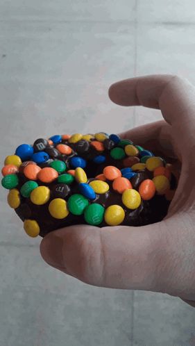 a person is holding a chocolate donut with m & m 's on it