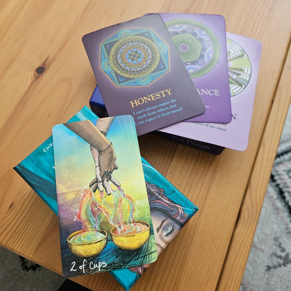 Two card deck boxed on a wooden tabletop - one has the 2 of Cups card laying on top of it from the Light-Seer's Tarot deck and the other has 3 purple oracle cards from the Soul's Journey oracle deck. The Honesty card is the only one legible.