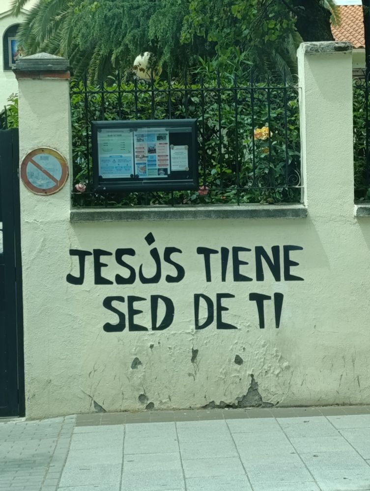 Foto del muro de una iglesia. En la parte de abajo pone "JESÚS TIENE SED DE TI".
