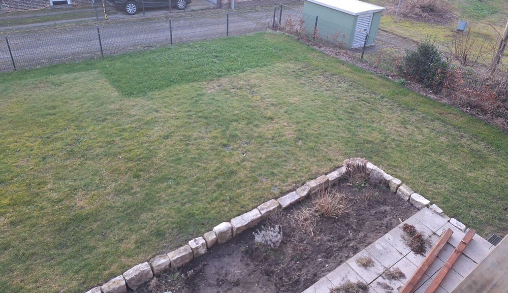 Rechter Teil des Gartens, wie mittlerer Teil, nur mit Terrassenecke vorne im Bild und TrafoHäuschen und Gestrüpp auserhalb des Grundstücks, hinter dem halbhohen, durchsichtigen Stabmattenzaun.