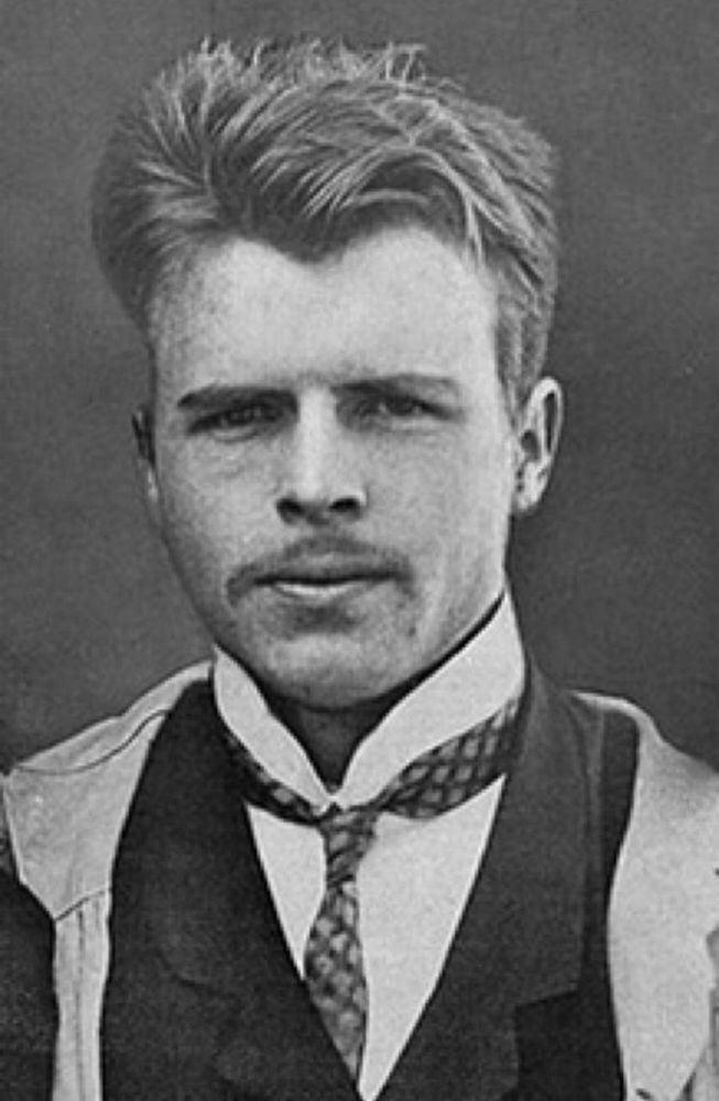 Auf dem Foto sieht man einen jungen Mann mit einem schmalen Gesicht, einem kleinen Oberlippenbart. Seine Haare stehen ziemlich vom Kopf ab