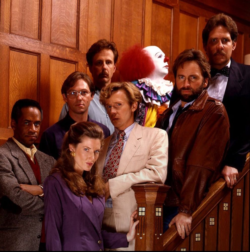 Cast of It staring intently at the camera while Pennywise looks off distracted
