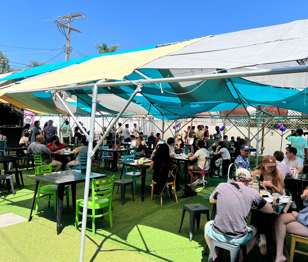 A crowd hanging out around tables on a shaded patio