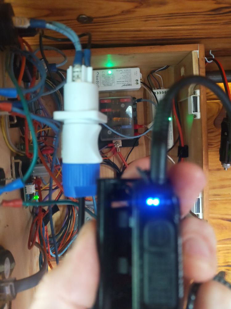 une prise qui pendouille d'un tableau électrique, il y a une lampe frontale branchée dessus et une lumière indique qu'elle charge