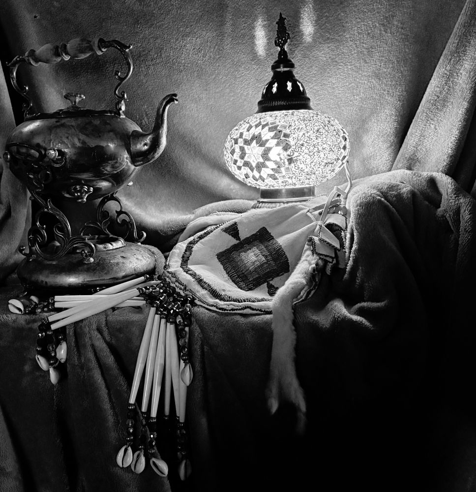 This is a black and white photo still life I took, months ago. I titled it “Selfie,” because it’s things that represent me: the beaded purse my mom made for me to carry at Native American pow wows when I danced as a kid, a hippie-style lamp, and a Victorian era tea kettle where the kettle is over a candle holder so the flame warms the tea. 