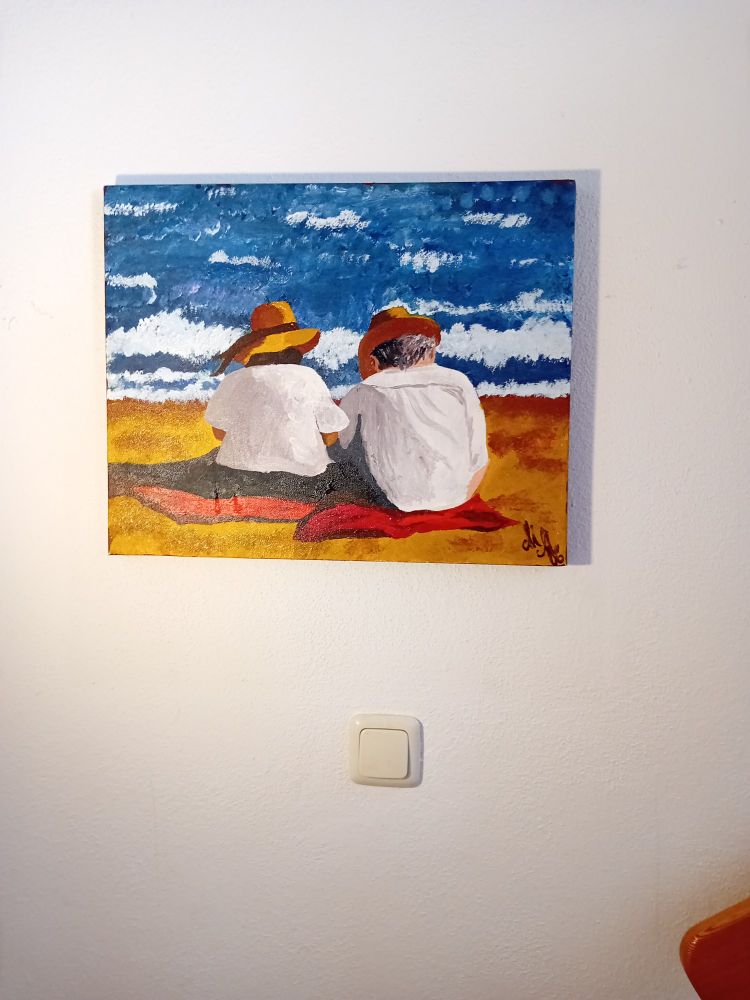 Gemälde von Michaela Charlesworth. 2 ältere Leute sitzen auf Decken am Strand und lesen. Beide haben Strohhüte auf und der Oberkörper ist weiß gekleidet.