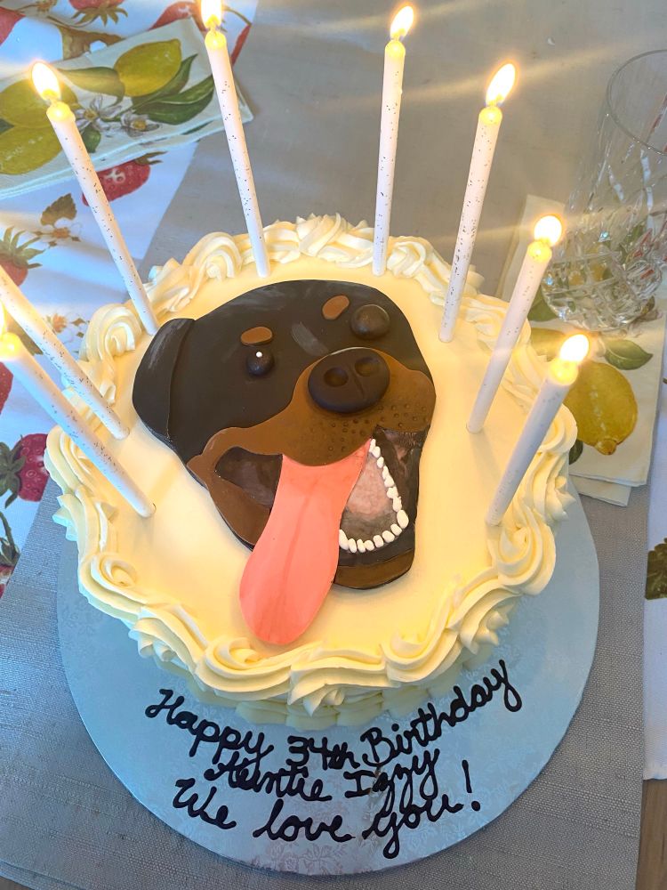A birthday cake with 8 lit candles. In the centre is the face of a Rottweiler. 