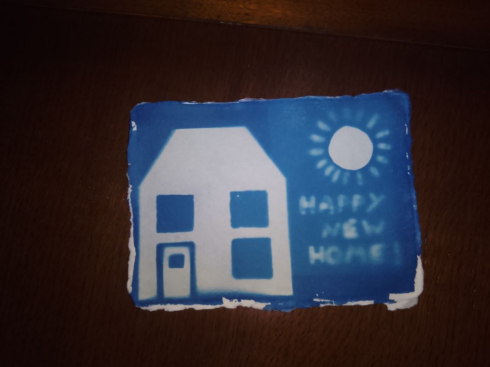 A cyanotype "new home card" showing a house and a sun, white against blue.