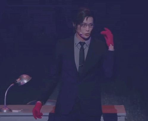 a man in a suit and tie with red gloves is standing in front of a desk