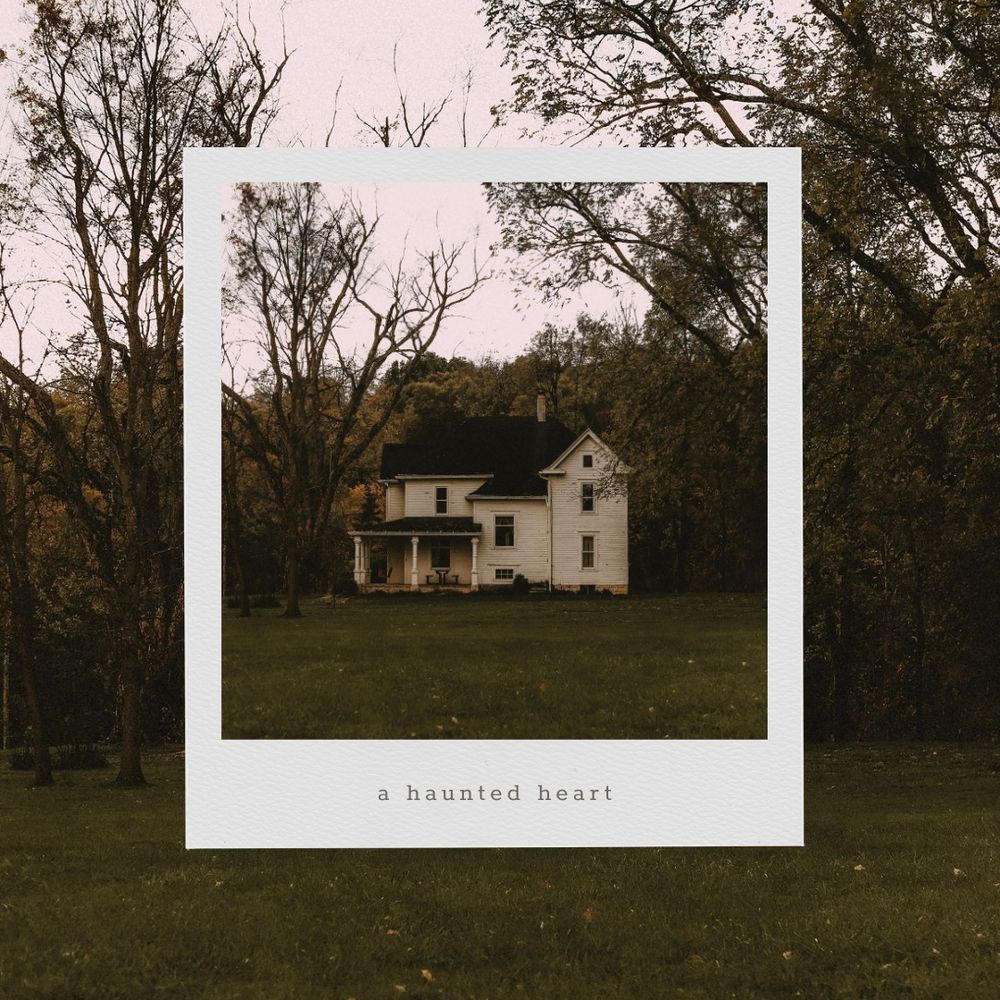 moodie for 'a haunted heart' that is a photo of a house—a very stereotypical farmhouse you would find in New England with aged cream paint over two stories and a partial wraparound porch—is laid over a larger picture that is the exact same picture. The house seems lonely—partially due to it being all alone on a relatively big lot and partially due to the lighting. It appears to be autumn at dusk.