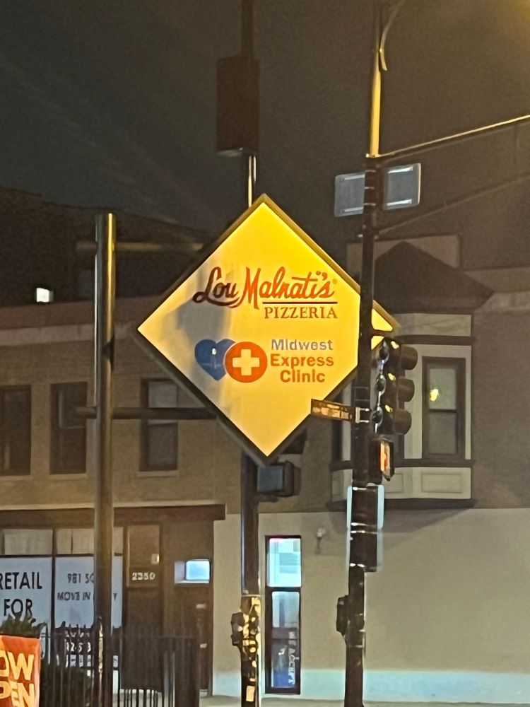 A photograph of a sign at night, lit by the distinctive yellow glow of Chicago’s streetlights.
The sign shows two businesses side by side: a Lou Malnati’s (pizza shop) and a Midwest Express Clinic (urgent care).