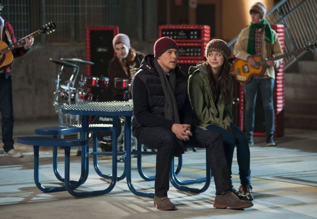 Finn and Marley from Glee sitting outside at a lunch table, dressed for chilly weather. There are two guitarists and a drummer behind them, also bundled up, beginning to play as Finn starts singing "Don't Dream It's Over" by Crowded House.