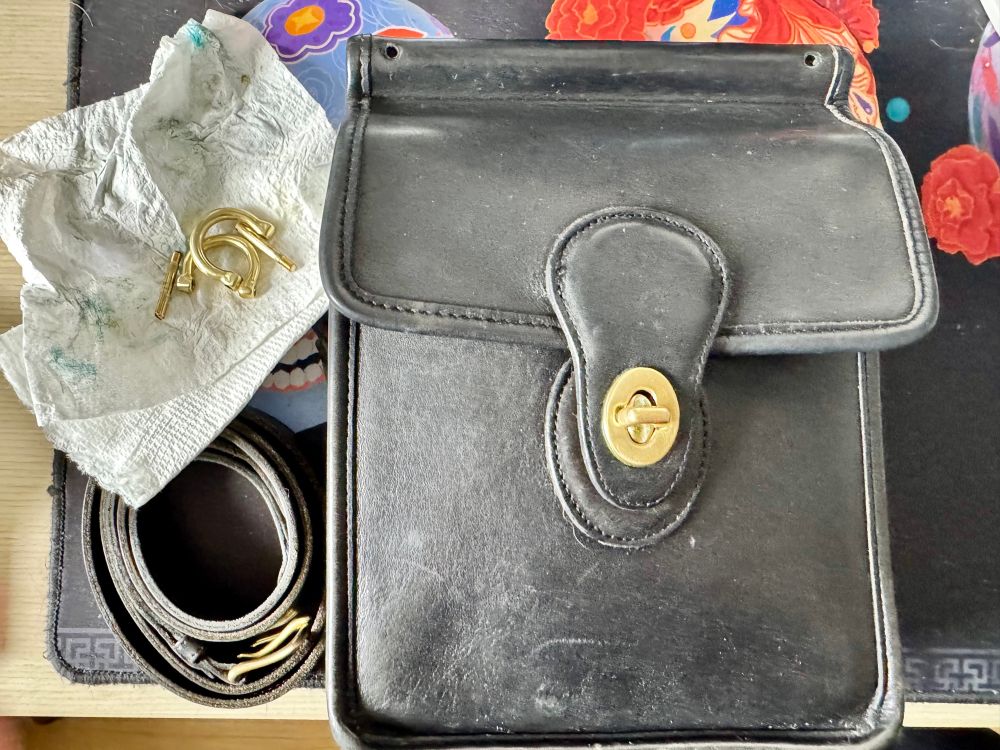 A disassembled black Coach Murphy bag, with brass hardware in the process of being polished. 