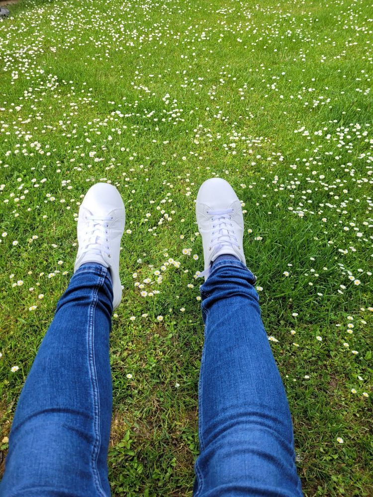 Beine in Jeans und weißen Sneakers schaukeln, über grünem Rasen mit Gänseblümchen.
