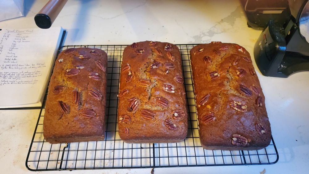 3 loaves of banana bread, topped with pecans, on a cooling rack