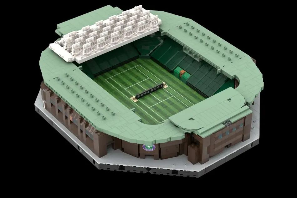 A detailed LEGO model of a tennis stadium with green seating and a central grass court, viewed from above. The model includes a covered area and spectator stands.