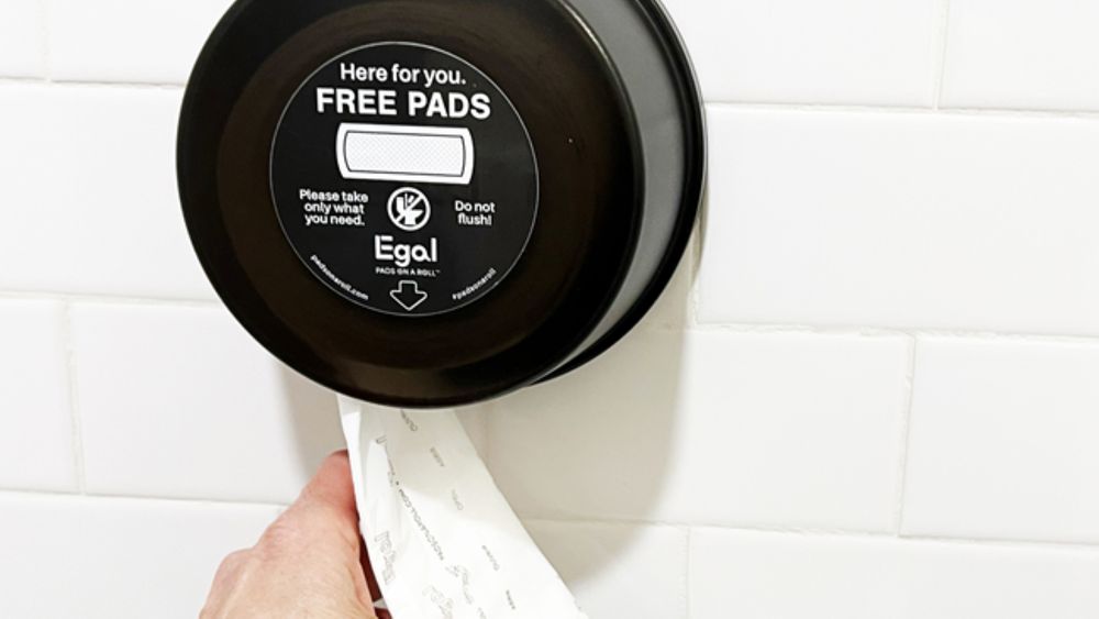 Egal Pads on A Roll dispenser is pictured. A hand is seen rolling out a pad for use.